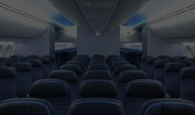 Interior of an airplane cabin showing rows of dark blue seats and overhead compartments